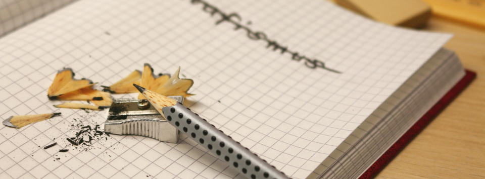 Ein Bleistift und ein Spitzer liegen auf einem Notizbuch.