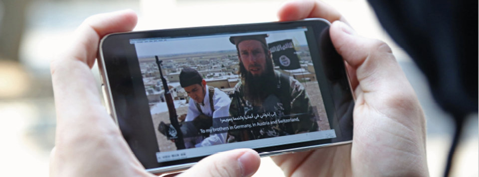 Zwei Hände halten ein Smartphone, auf dem ein Videoausschnitt zweier Kämpfer des Islamischen Staates zu sehen ist.