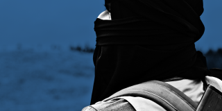 Ein vermummter Mann mit Maschinengewehr auf dem Rücken schaut in die Ferne.