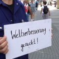 Ein Mann hält ein Schild mit dem Schriftzug Weltverbesserung gesucht!